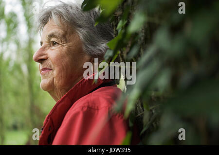 Donna anziana appoggiata su albero in posizione di parcheggio Foto Stock