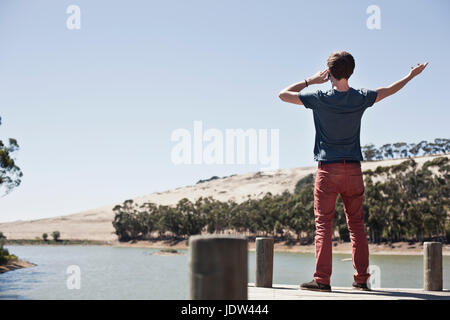 Vista posteriore del giovane uomo su telefono cellulare, affacciato sul lago di scena Foto Stock