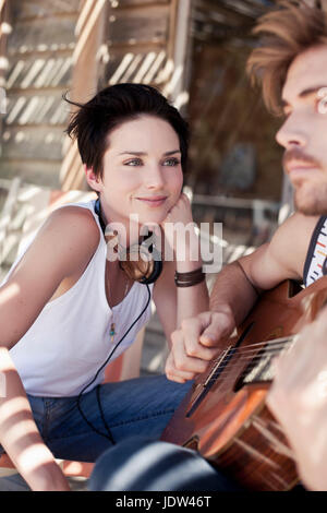 Giovane donna guardando il suo ragazzo a suonare la chitarra Foto Stock