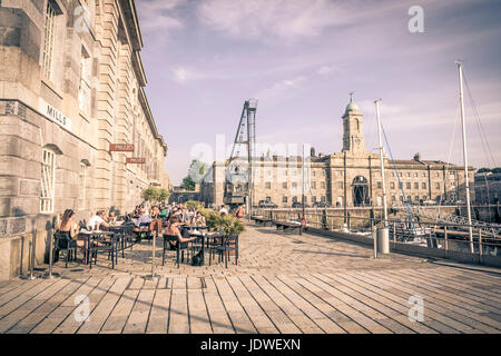 Alfresco diners gustando cibi e bevande nella luce del sole. Le piantatrici di fiori e i tavoli e le sedie fuori Prezzo Ristorante Royal William Yard, Plymouth Foto Stock