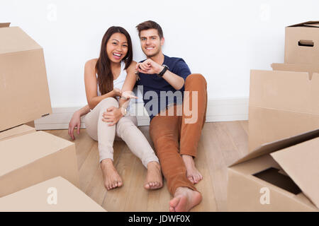 Ritratto di giovane coppia multietnica seduto sul pavimento tenendo premuto il tasto dalla loro nuova casa Foto Stock