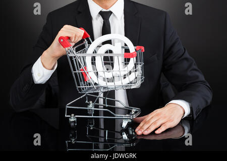 Sezione mediana del giovane imprenditore con carrello modello e a firmare al banco su sfondo nero Foto Stock