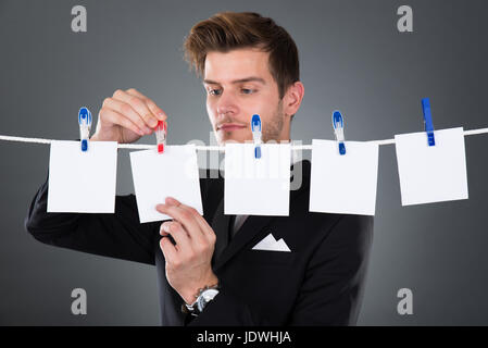 Giovane imprenditore pinning fogli vuoti su stendibiancheria contro uno sfondo grigio Foto Stock