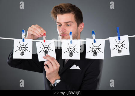Giovane imprenditore carte pinning lampadine su stendibiancheria contro uno sfondo grigio Foto Stock