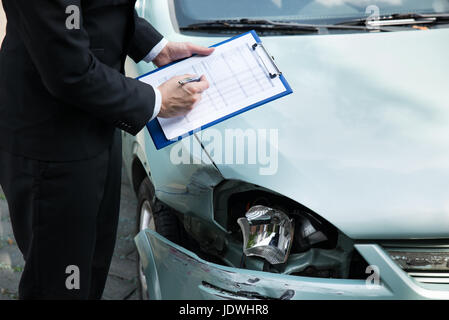 Sezione mediana di scrittura sulla clipboard mentre agente di assicurazione auto di ispezione dopo un incidente Foto Stock