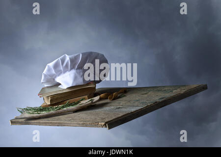 Vecchi libri di culinaria , chef hat e cucchiai di legno . Accessori da cucina sul vecchio tavolo in legno nel cielo. Foto Stock
