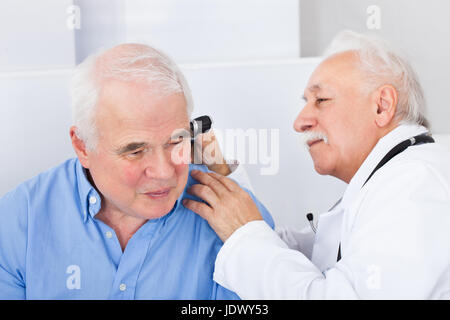 Sorridente medico maschio esaminando senior uomo l orecchio con otoscopio in clinica Foto Stock