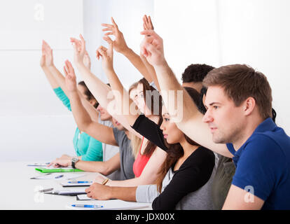 Fila di multietnica studenti del college alzando le mani in aula Foto Stock