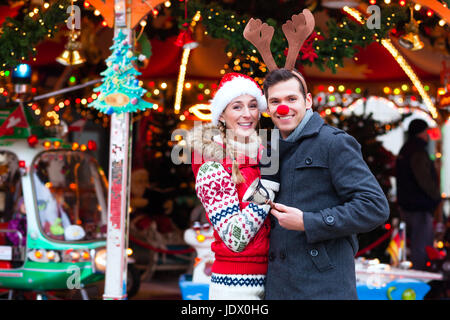 L uomo e la donna o una coppia o amici durante il tempo di avvento o vacanze a fronte di una giostra o 'marry-go-round' sul Natale o mercatini di Natale Foto Stock