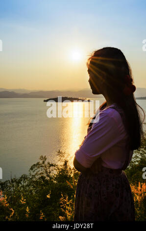 Felice giovane donna in piedi sulla collina a guardare il tramonto sul lago in Kaeng Kra Chan National Park, Phetchaburi Provincia, Thailandia Foto Stock