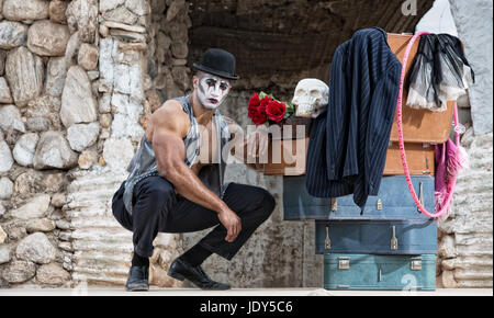 Bello il cirque muscolare attore inginocchiato accanto ai bagagli Foto Stock