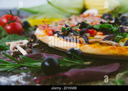 La pizza italiana con mozzarella di bufala, olive nere, il prosciutto e i pomodori Foto Stock