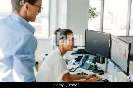 Donna d'affari matura che lavora al computer con un collega maschio in attesa. uomo d'affari e donna alla scrivania che guarda il monitor del computer. Foto Stock