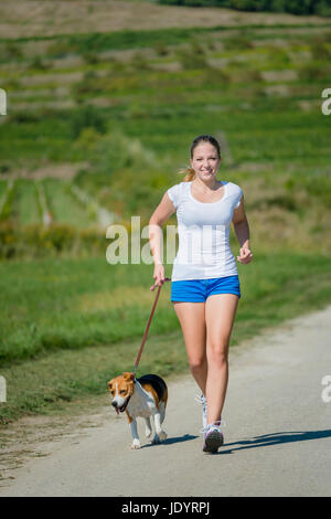 Bella ragazza adolescente jogging con il suo animale domestico (cane beagle) in natura Foto Stock