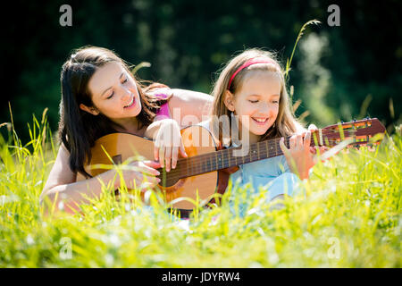 La Madre insegna chitarra plaing il suo bambino - outdoor in natura sulla giornata di sole Foto Stock