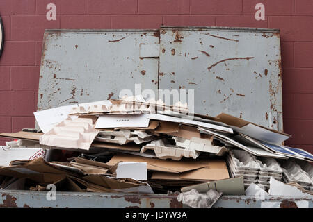 Chiusura del cassonetto riempito con del cartone per il riciclaggio. Coperchio aperto contro la parete rossastra. Orizzontale. Foto Stock