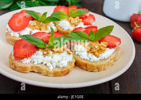 Mini sandwich con ricotta e fragole fresche e decorate con foglie di menta sul pane di segale su legno scuro dello sfondo. Una corretta alimentazione. Healt Foto Stock