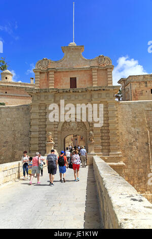 I turisti a piedi oltre il fossato bridge attraverso il portale di ingresso della città medievale di Mdina, Malta Foto Stock