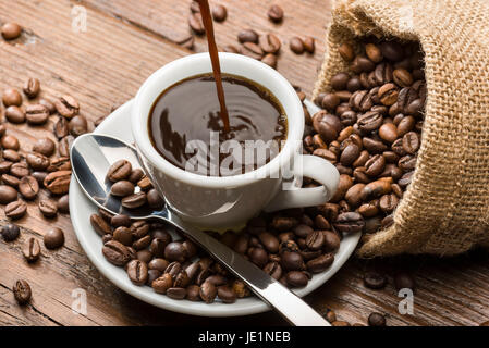 ciambella, tazza di caffè fumante con latte art e chicchi di caffè sul  tappetino di tela su un tavolo in legno e sfondo nero 2009154 Stock Photo  su Vecteezy