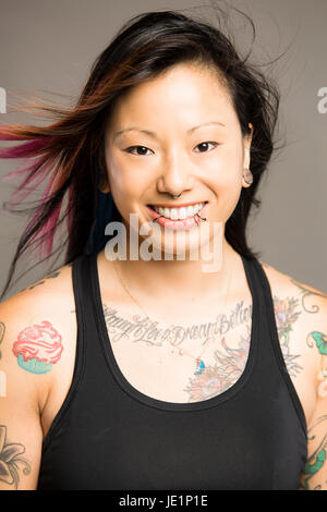 Giovane donna asiatica con i capelli colorati e tatuaggi e piercing sorrisi a viewer Foto Stock