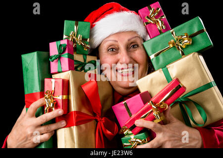 Gioioso lady senior con Babbo Natale cappuccio è abbracciando una dozzina di avvolgere i regali di Natale. Tutti confezionati in monocolore oro, rosso e verde. Isolato su sfondo nero. Dicembre idea regalo tema. Foto Stock