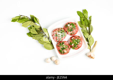 Cibo crudo, manzo cotoletta pronto per preparare con aglio e foglie di alloro. Carni macinate in scatola di plastica su sfondo bianco. Foto Stock