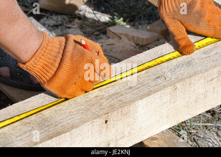 Costruzione cottage di legno. Misurazione di barre di pino con l aiuto di un metro di vintage strumento closeup all'aperto. Foto Stock