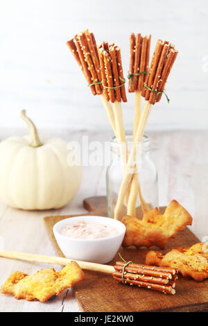 Antipasti rustico per una festa di Halloween con le streghe broomsticks realizzato da grissini e salatini e bat cookies o biscotti serviti con una saporita dip con un bianco autunno dietro di zucca Foto Stock