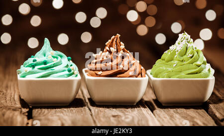 Coloratissima fila di tre differenti frozen yogurt dessert in blu, marrone e verde guarnito con dadi e perle di zucchero ad una festa con una scintillante sfondo bokeh di luci Foto Stock