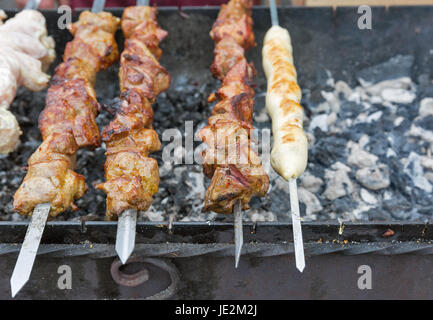 Stuzzicanti spiedini e shish kebab arrostito su spiedini, closeup all'esterno. Cucina di strada. Foto Stock