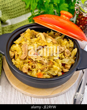 Stufato di cavolo con la carne in un nero la pentola con un coperchio, igienico, pepe, prezzemolo. cucchiaio su uno sfondo di scheda di luce Foto Stock