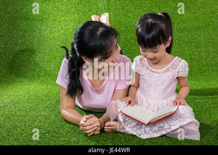 Asian madre cinese e la figlia sdraiati sull'erba e la lettura del libro al parco all'aperto Foto Stock