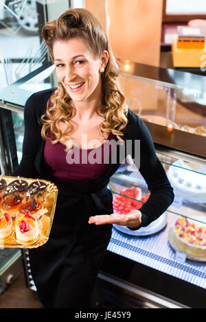 Pasticceria femmina presentando il vassoio della torta nel forno o pasticceria Foto Stock