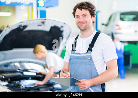 Maschio e femmina team meccanico esaminare auto a motore con la luce e la lista di controllo in officina Foto Stock