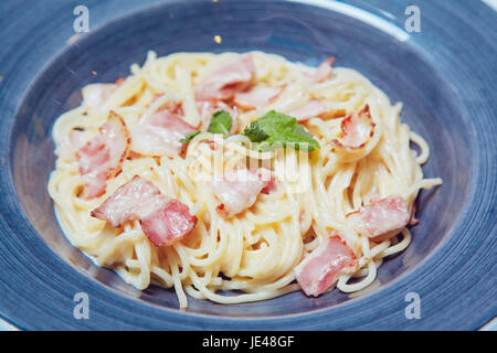 Spaghetti alla carbonara con pancetta e formaggio sulla piastra di blu. Foto Stock