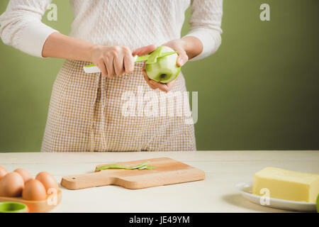 Casa moglie indossando il grembiule. Fasi di Realizzazione di cottura di torta di mele. Il taglio di mela verde. Foto Stock