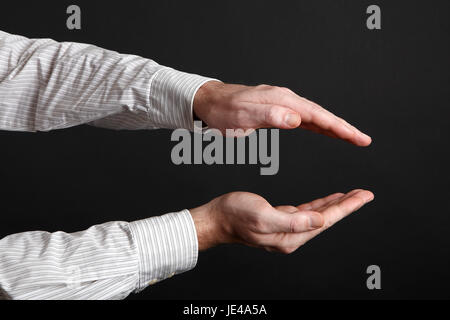 Maschio caucasico mani proteggere qualcosa davanti a uno sfondo nero Foto Stock