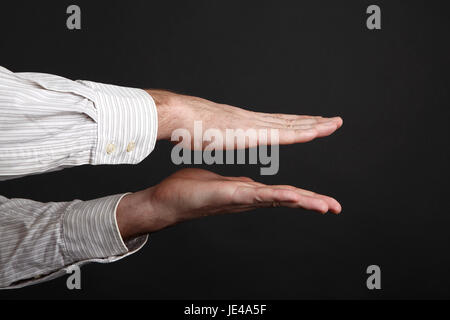 Maschio caucasico mani spremere qualcosa davanti a uno sfondo nero Foto Stock