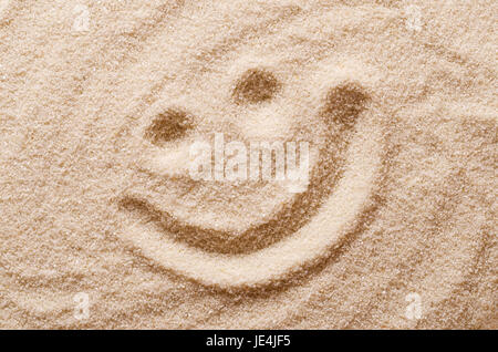 Felice volto sorridente nella sabbia. Gli occhi e la bocca disegnata con un dito asciutto ocherous sabbia. Foto macro close up dal di sopra. Foto Stock
