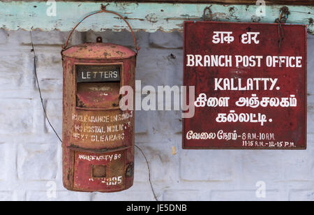 Nilgiri Hills, India - 26 Ottobre 2013: primo piano della cassetta postale arrugginito e segno a Kallatty Post Office. Scrittura in bianco su rosso segno in Tamil e in inglese. Gr Foto Stock