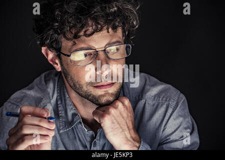 Uomo con penna e guardando verso il basso con la mano sotto il mento Foto Stock