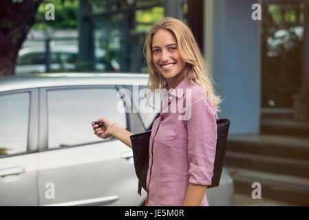 La donna si avvicina auto con chiavi in mano, sorridente sulla spalla Foto Stock