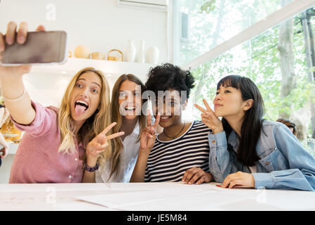 Gli amici utilizzando smartphone per prendere selfie in cafe Foto Stock