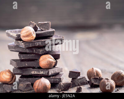 Pila di cioccolato fondente e nocciola intera con copia spazio. Cioccolato con le briciole e le nocciole su sfondo di legno. Foto Stock