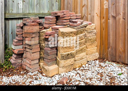 Usarono mattoni e pietre per pavimentazione impilate contro la recinzione di legno con ghiaia bianca in primo piano. Orizzontale. Foto Stock