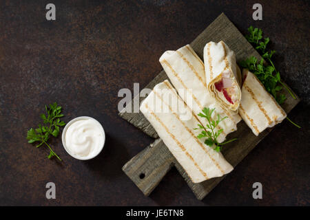 Shawarma pane pita con pollo alla griglia, verdure fresche e salsa alla panna su uno sfondo di colore marrone pietra. Vista da sopra con copia spazio. Foto Stock