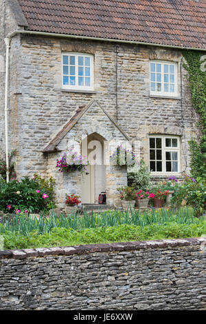 Cottage in pietra e floreali cestelli appesi e giardino frontale a Coln St Aldwyns. Cotswolds, Gloucestershire, Inghilterra Foto Stock