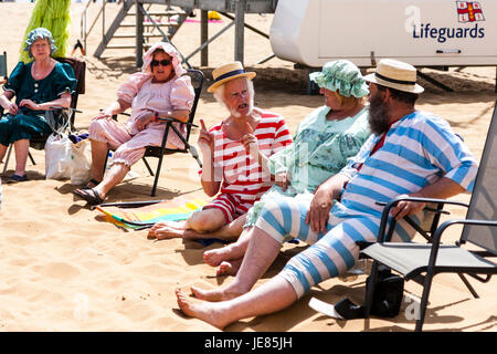 Fila di cinque matura e personale senior in seduta piegare su sedie a Broadstairs sands. Tutti vestiti in stile vittoriano costumi da bagno come parte di Dickens settimana. L'uomo in mezzo a parlare e utilizzando le mani per mostrare la lunghezza di qualcosa. Quello che ha preso il via? Foto Stock