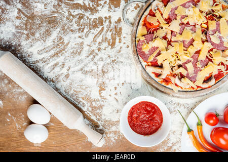 Vista superiore della pizza ingredienti, pomodori, salame e funghi sul piano portapaziente in legno Foto Stock