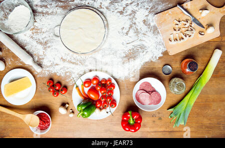 Vista superiore della pizza ingredienti, pomodori, salame e funghi sul piano portapaziente in legno Foto Stock